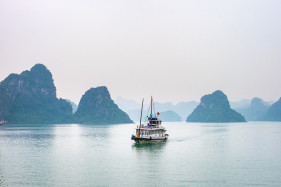 A boat passes through foggy karst landscape in Ha Long Bay, Quảng Ninh Province, Vietnam