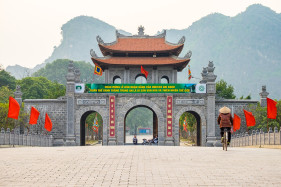 A Vietnamese woman rides a bicycle in front of the gateway to Hoa Lư, ancient capital of Vietnam, Ninh Bình Province, Vietnam