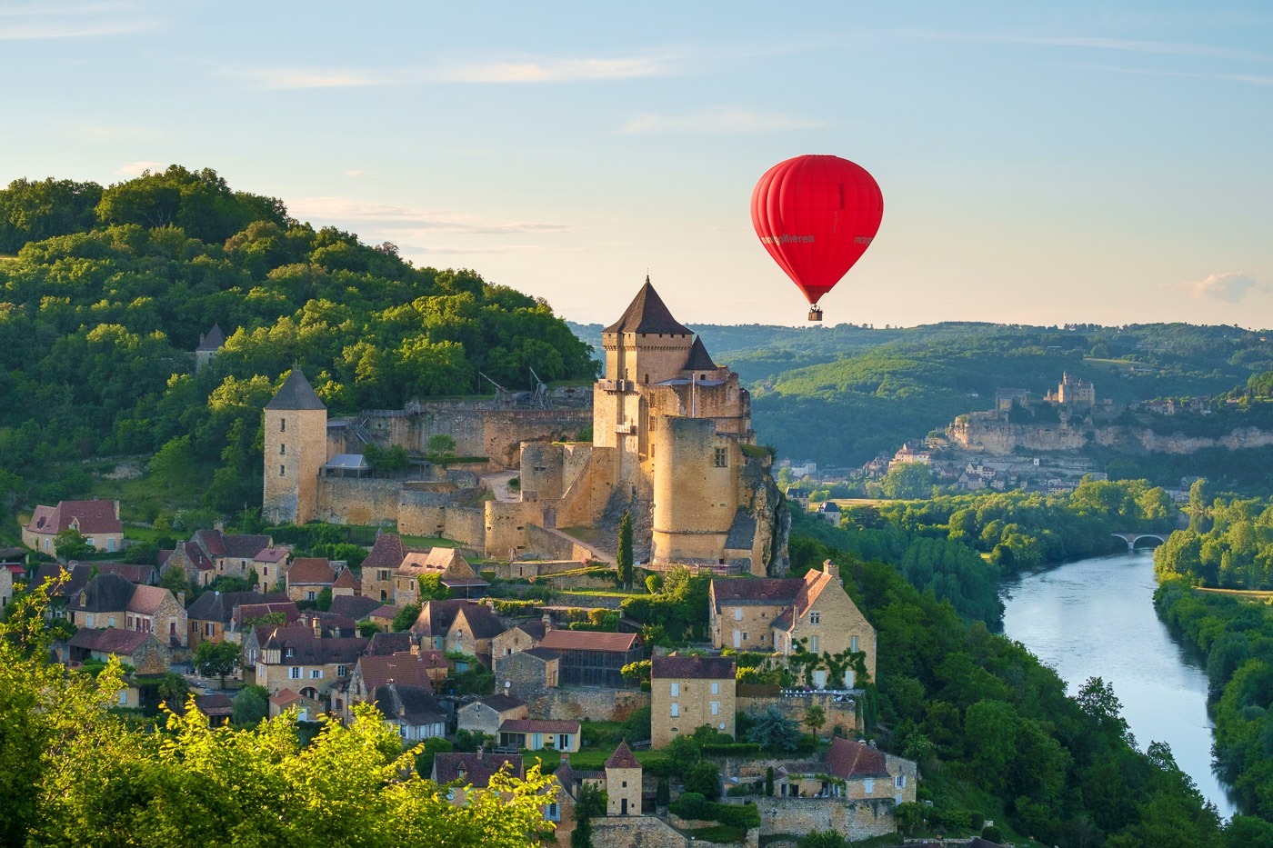 Hot-air balloon over Chateau de Castelnaud castle and Dordogne River valley in late afternoon